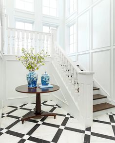 two vases with flowers sit on a table in front of a staircase leading up to the second floor