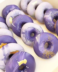 purple donuts with sprinkles and gold flakes in a white box