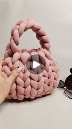 a hand holding a pink purse with eyeglasses on the table next to it