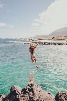 a woman jumping into the ocean from rocks