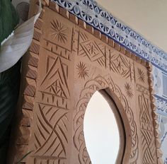 a close up of a carved wooden object with a plant in the foreground and a wall behind it