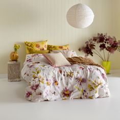 a bed with white sheets and colorful flowers on the comforter next to vases