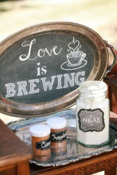 a sign that says love is brewing next to some jars with candles in them on a table