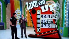 two men standing next to each other in front of a big screen tv set with numbers on it