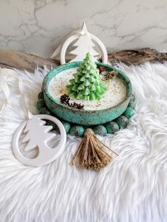 a bowl with a christmas tree in it on a white fur covered surface next to other items