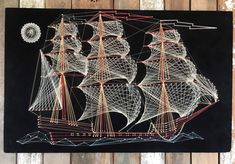 a drawing of a sailing ship on a black board with red and white string art