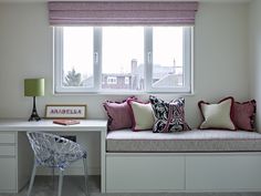 a window seat with pillows on it next to a desk