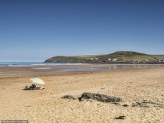 two people are sitting under an umbrella on the sand at the beach near the ocean