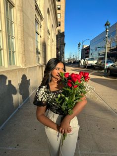 a woman standing on the sidewalk with flowers in her hand