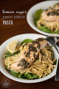 two white bowls filled with pasta and salmon on top of a wooden table next to silverware