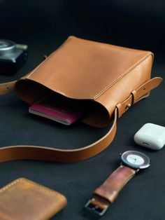 a brown leather bag sitting on top of a table next to an apple watch and wallet