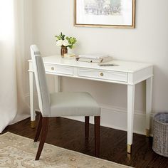 a white desk and chair in front of a window with a painting on the wall