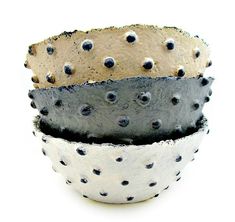 three ceramic bowls with holes in them sitting on a white surface, one is black and the other is grey