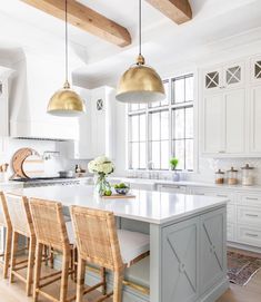 a large kitchen with white cabinets and gold pendant lights over the island countertop, along with wicker chairs