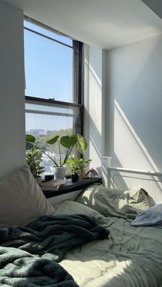 an unmade bed sitting in front of a window with plants on top of it