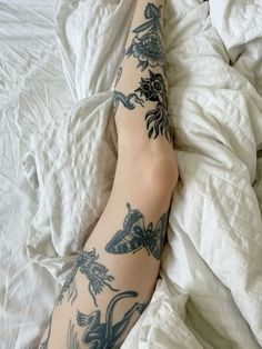 a person with tattoos on their legs laying in bed next to sheets and pillows,