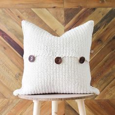 a white pillow with buttons on it sitting on a wooden stool in front of a wood wall