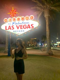 a woman standing in front of the welcome to fabulous las vegas sign at night time