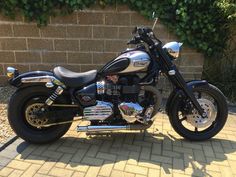 a black motorcycle parked on top of a brick road next to a wall and bushes