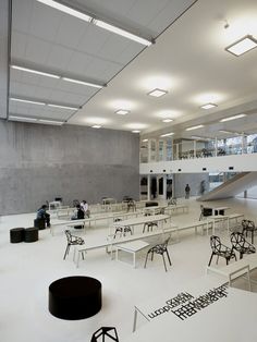 an empty room with tables and chairs in the center, some people are walking around