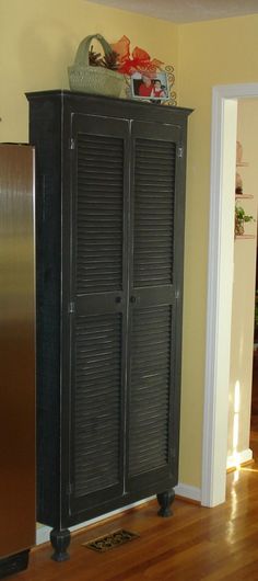 a black cabinet sitting on top of a hard wood floor next to a metallic refrigerator