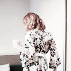 a woman standing in front of a mirror wearing a robe and holding a coffee cup