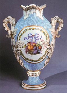 a blue vase with gold trimming and fruit painted on the sides, sitting on a table