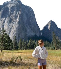 a woman standing in front of a mountain with her back to the camera and looking at it