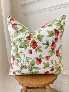 a white pillow with strawberries on it sitting on a wooden chair next to a window