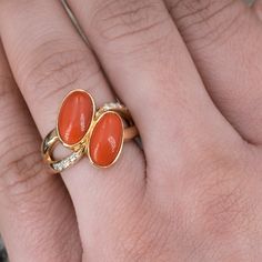 This gorgeous coral ring is centered with two (2), bezel set, oval cabochon cut natural coral. The ring features a split shank design and is accented with eight (8), bead set, round brilliant cut diamonds. The ring measures 18.1mm at the top, rises 5.7mm above the finger, tapering to 2.9mm wide and 1.3mm thick at the base of the shank. "K18 D0.11" is stamped on the inside shank. The ring is currently a size 6.5. Elegant Multi-stone Orange Rings, Elegant Orange Multi-stone Rings, Elegant Coral Ring Jewelry, Coral Oval Jewelry For Weddings, Elegant Oval Coral Rings, Elegant Coral Rings For Anniversary, Elegant Coral Oval Rings, Elegant Oval Coral Jewelry, Elegant Coral Oval Jewelry