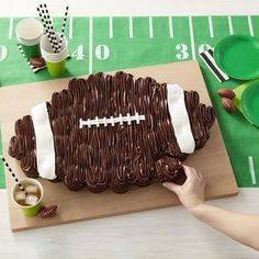 a football shaped chocolate cake sitting on top of a cutting board next to plates and cups