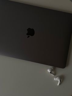 an apple laptop computer sitting on top of a white table next to earbuds