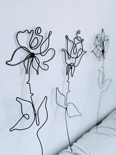 three metal flowers sitting on top of a white couch next to a wall mounted art piece