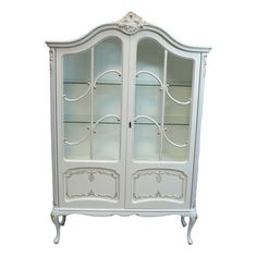 a white china cabinet with glass doors and ornate carvings on the front, against a white background