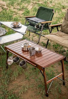 an outdoor table with pots and pans on it next to two chairs in the grass