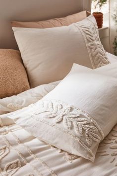 a bed with white linens and pillows on it's headboard, next to a potted plant