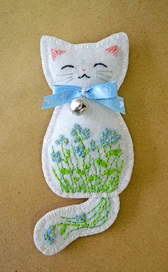 a white cat with a blue bow on it's collar and tail sitting next to a bell