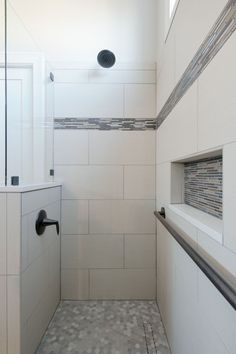 a walk in shower sitting next to a white tiled wall and counter top under a window