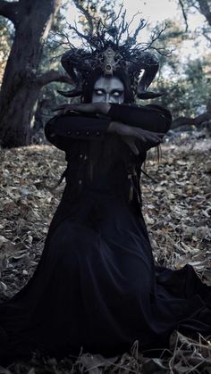 a woman dressed in black is sitting on the ground with her hands over her face