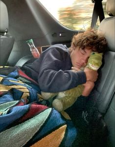 a young boy laying in the back seat of a car holding a stuffed alligator toy