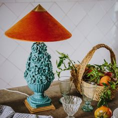 a blue lamp sitting on top of a wooden table next to a basket of fruit