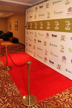 a red carpeted area with barriers and signs on the wall in front of it