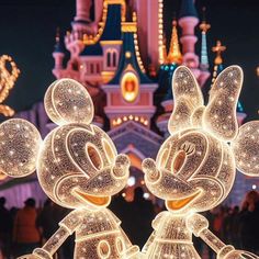 lighted mickey and minnie mouse statues in front of a castle