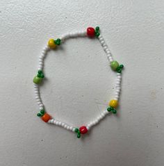 a white beaded bracelet with green, yellow and red beads is displayed against a white wall