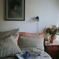 a bed covered in pillows and blankets next to a window with a painting on the wall