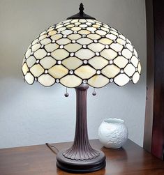 a table lamp sitting on top of a wooden desk next to a white vase and wall