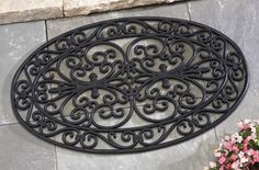 a large metal door mat sitting on top of a stone floor next to flowers and potted plants