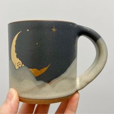 a hand holding a coffee cup with a painting on the outside and gold stars in the sky