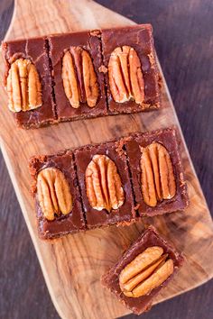 three pieces of chocolate with pecans on top and one piece cut in half sitting on a wooden cutting board