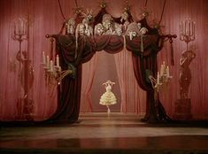 a woman standing in front of a red curtain with skulls on it and chandelier